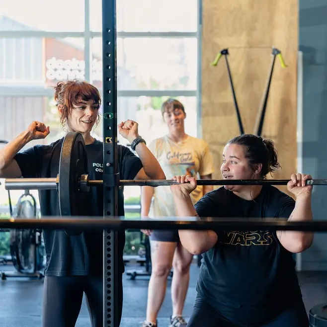 Coach cheering on a member squatting a barbell during a personal training session in Ballard, Seattle